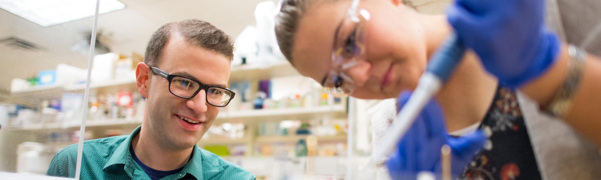 Photo of GVSU Biochemistry student working in a lab with a faculty member assisting.